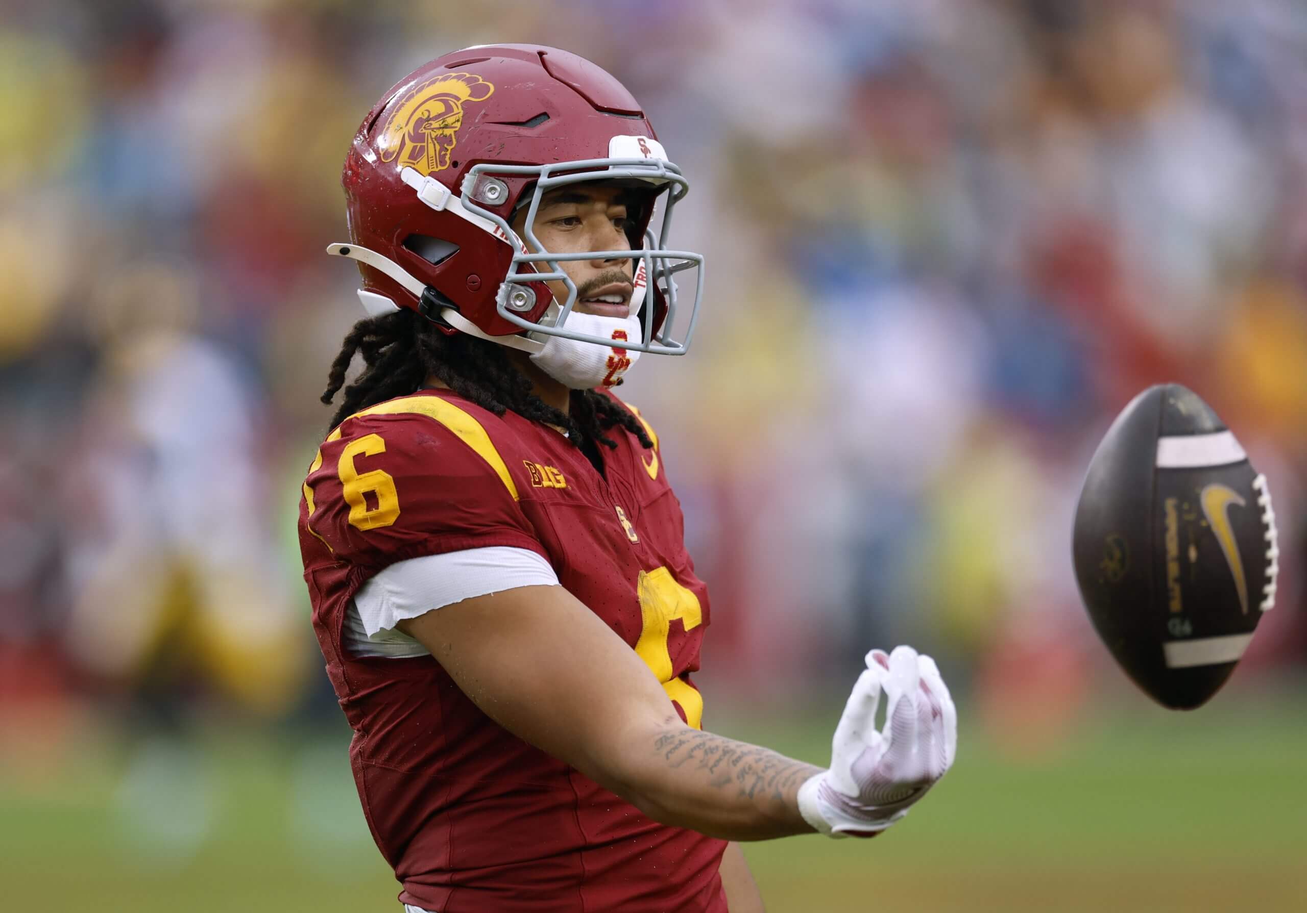 Makai Lemon, wearing a red No. 6 uniform, smiles and holds his right arm out to the side after flipping the football away.