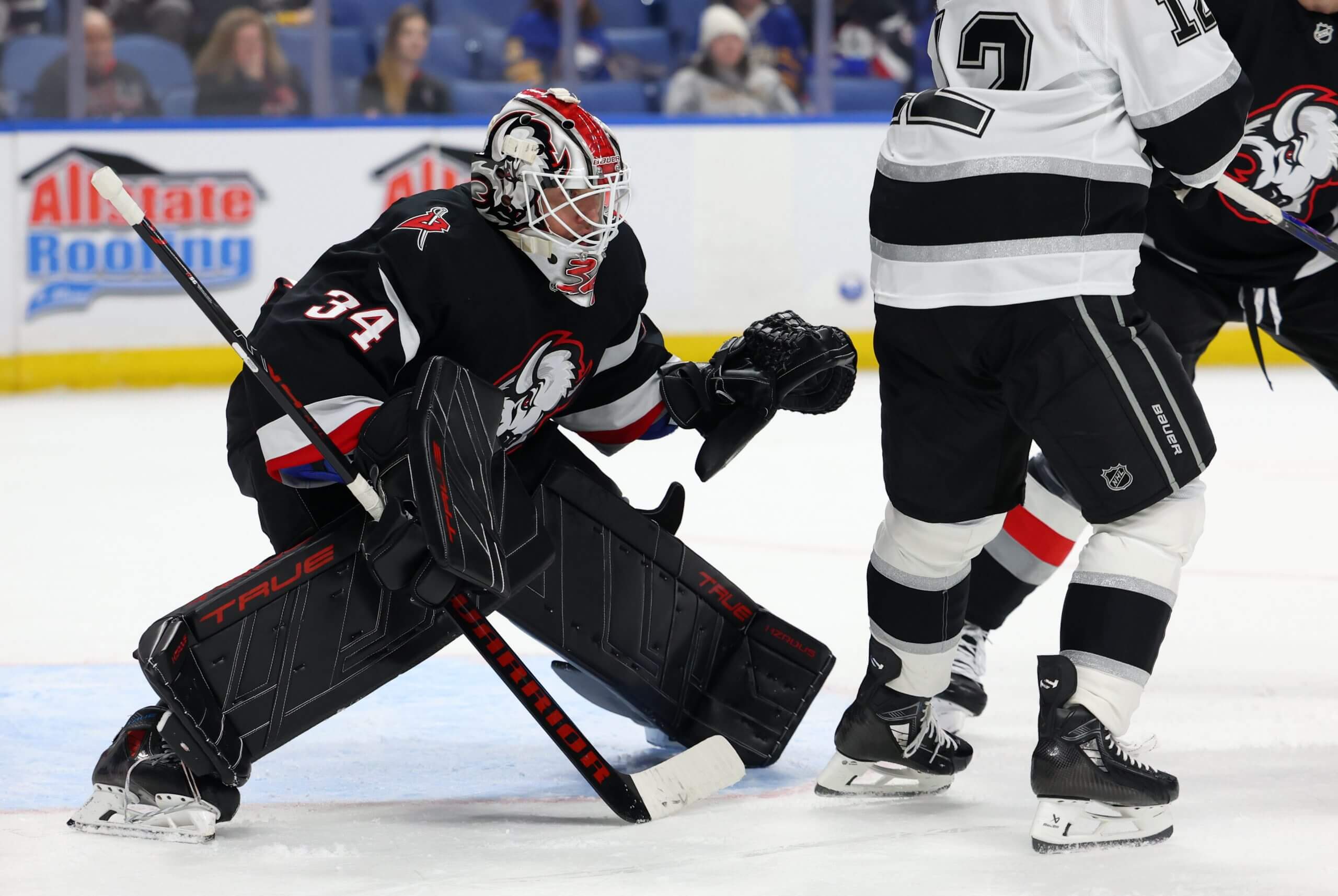 Alex Lyon crouches in the Buffalo net with a Kings player near the crease.