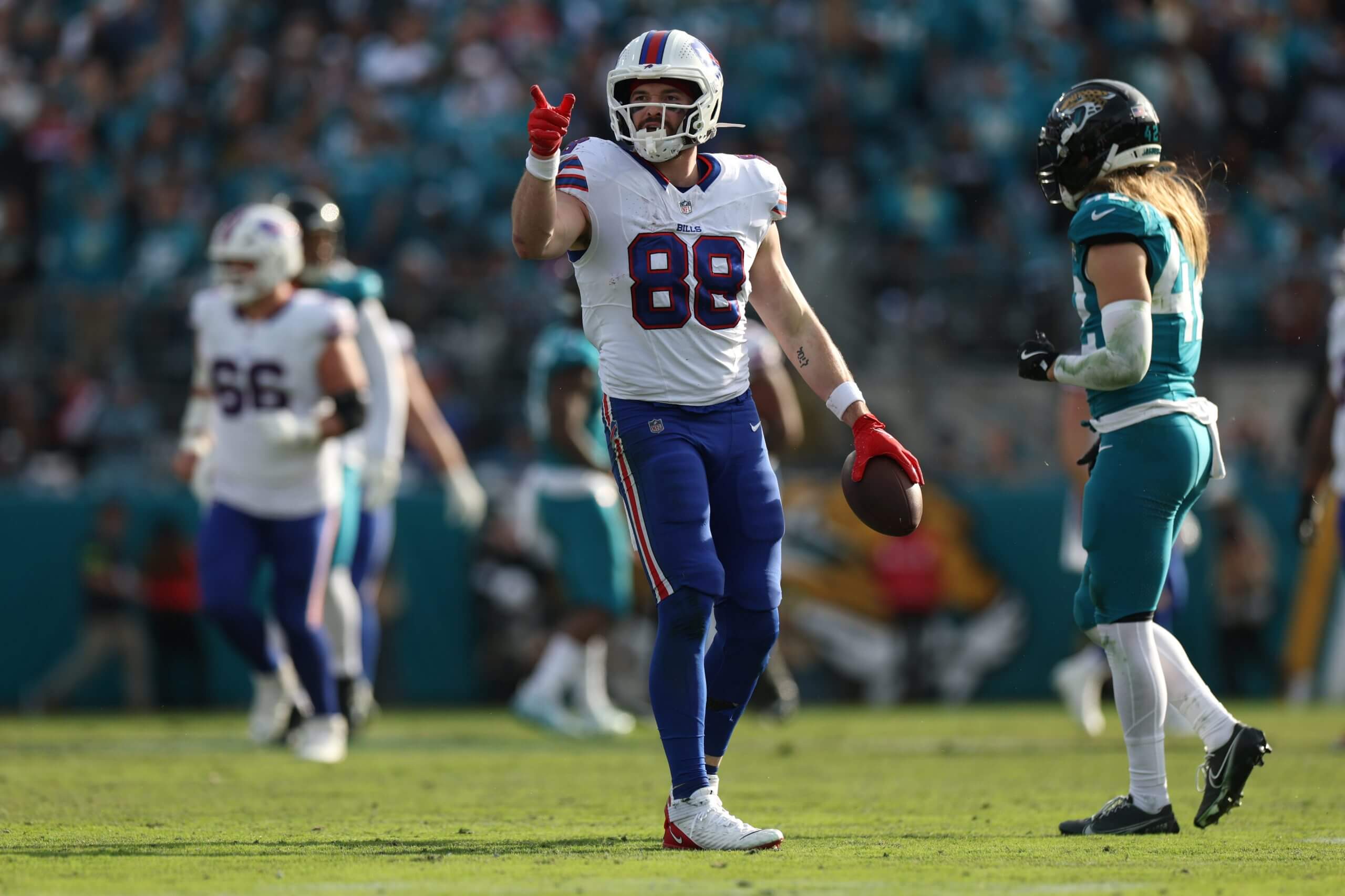 Dawson Knox, in a No. 88 jersey, holds the football with his left hand and points with his right hand.